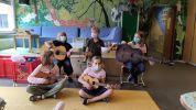 Kinder sitzen mit Gitarren in einem bunt bemalten Raum und musizieren gemeinsam.