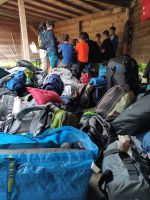 Gruppe von Kindern sitzt in einer Holzhütte um einen Tisch, davor liegen viele Rucksäcke und Taschen.