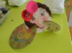 Bunte Collage aus Papier mit gemaltem Gesicht und runden, farbigen Flächen auf grünem Tisch.