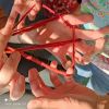 Mehrere Hände spielen das Fadenspiel mit roter Wolle, Sonnenlicht fällt auf die Szene.